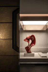 A large, curved glass sculpture in a room with a white wall and a light source highlighting its design