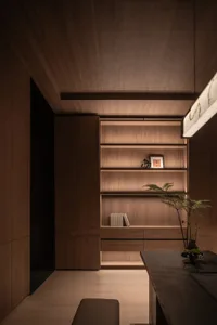A well-lit room with wooden walls, a wooden bookshelf filled with books, and a potted plant on the floor