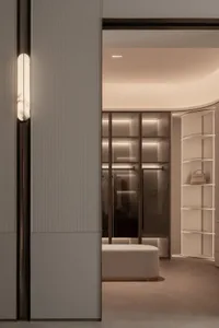 A dimly lit bedroom with a white color scheme, featuring a bed, closet, and bench in a clean and minimalist space