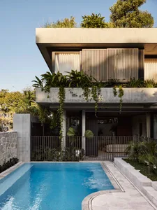 A modern house with a large window, balcony, and blue swimming pool surrounded by a patio and potted plants, with natural light and a clean, minimalist design