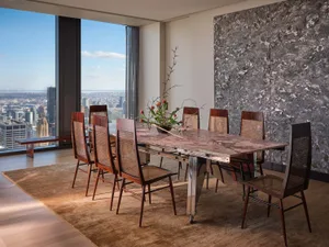 A modern dining room with a large window, a dining table, chairs, and a vase with flowers, set for a meal, with a view of the city