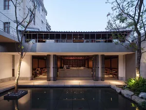 A modern restaurant with a pond in the center, large windows, and comfortable seating areas