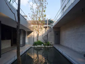 A modern architectural scene featuring a large open space with a concrete staircase and a pond, surrounded by natural light and windows