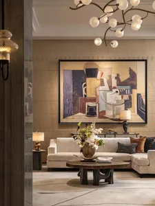 A modern living room with a couch, chair, and dining table, featuring a large painting, wood furniture, and glass accents, with natural and lamp lighting, creating a warm and inviting atmosphere