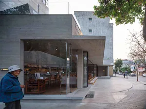 Modern restaurant interior with a large glass wall, wooden tables, and chairs, flooded with natural light