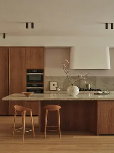 Modern kitchen with wooden cabinets, marble countertop, sink, oven, microwave, and decorative vase