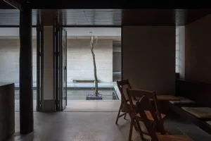 餐廳區域中央擺放一棵大樹，周圍環繞著餐椅與餐桌，木質地板搭配玻璃門引進自然光線
