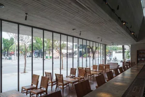 A modern restaurant space with wood furniture, high ceilings, and large windows allowing natural light to flood the area