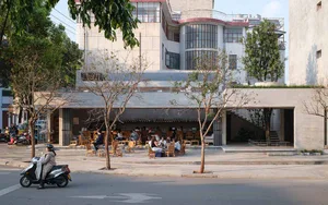 Outdoor restaurant with modern design, wood, and concrete elements, surrounded by people sitting at tables in a casual and relaxed atmosphere