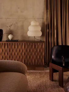 Cozy living room with a brown sofa, black chair, and a potted plant, set on a rug, with a table and lamp, in a well-lit space