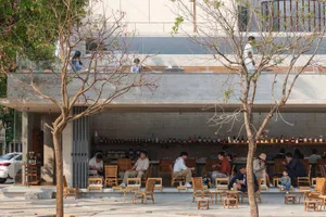 A modern restaurant with a mix of indoor and outdoor seating, featuring chairs, dining tables, and decorative lighting