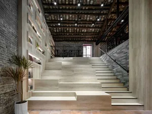 A modern staircase with a white railing and wooden steps, located in a room with a brick wall and a potted plant, under dim lighting