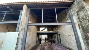 A group of people standing in a large, empty industrial building with stone and metal construction, featuring a brick-like texture on the walls