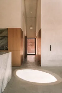 A modern kitchen and hallway area with white surfaces, a kitchen counter, dining table, and natural light from a window