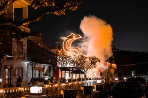 A restaurant building at night with a large illuminated bird statue on top, surrounded by dining tables and chairs