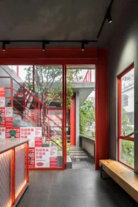 A modern residential space with a red staircase, red railing, and red door, featuring a window and a bench, with natural light streaming in