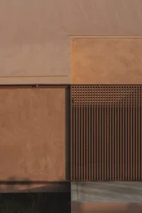 A modern building with a brown brick wall and a white wall, set against a natural background with warm and inviting lighting