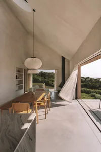 A bright and inviting open-concept living space with a wooden dining table, kitchen with sink and refrigerator, and natural light pouring in