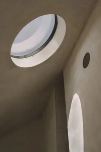 A small, dark room with a round window surrounded by a white frame, set against a concrete-like textured background