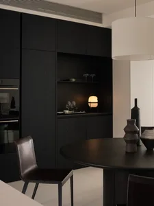 A modern kitchen with a dining table and chairs, surrounded by black furniture and wine glasses, under dim lighting