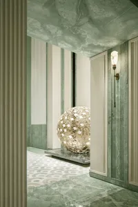 A modern hallway with a large gold ball on a pedestal, surrounded by a clean and modern space with a marble-like floor and soft, diffused lighting