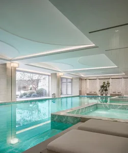 A modern pool area with a white tiled space, a white couch, and a well-lit pool surrounded by water