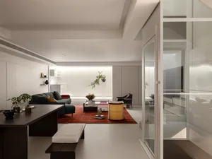 Modern living and dining space with a couch, chair, coffee table, dining table, and chairs, surrounded by potted plants, vases, and a bowl, with natural light from windows and wood and glass materials