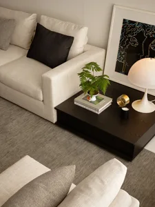 A well-lit living room with a couch, chair, coffee table, and potted plant, featuring predominantly white materials and a clean modern look