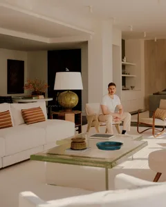 A well-furnished living room with a man sitting on a chair, surrounded by a couch, dining table, and vase, with a comfortable atmosphere