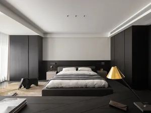 A dimly lit hotel bedroom with a black bed, chair, and gold lamp, creating a cozy atmosphere