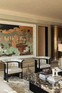 A well-lit living room with a couch, chair, and dining table, featuring a large painting on the wall