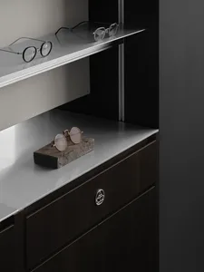 A dimly lit modern bedroom with a metal countertop, a bed in the background, and a pair of sunglasses and a small rock on the countertop