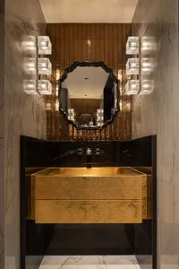 Modern bathroom with a gold-toned sink, mirror, and drawer, set against a black countertop, in a well-lit space with a warm and inviting atmosphere