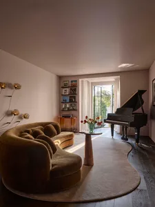 A dimly lit living room with a piano, couch, chair, dining table, and vases, featuring wood and fabric materials in a predominantly neutral color palette