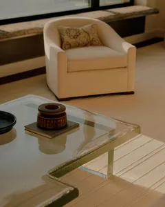 A modern living room with a white chair and glass coffee table, well-lit with natural sunlight and a warm atmosphere