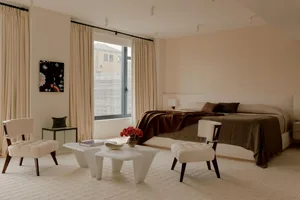 A bedroom with a bed, chair, table, and couch, featuring a large window for natural light and a cozy atmosphere