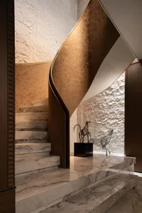 A modern staircase with a curved design, marble steps, and a wooden railing, set in a sophisticated hallway with a horse statue nearby