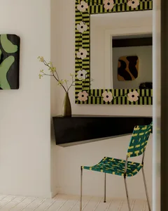 A well-lit living room with a black chair and mirror, a vase with flowers on a table, and a modern atmosphere