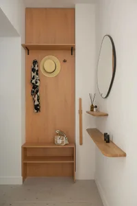 A cozy bedroom with a wooden shelf and mirror, featuring a bed in the background and various personal items on the shelf
