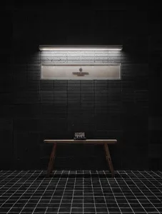 A dimly lit bathroom with a wooden bench and a mirror above it, set against a black tile floor