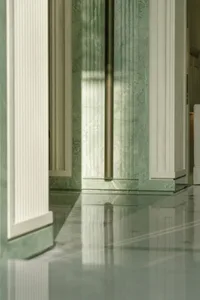 Green marble walls and floor in a dimly lit hallway with white columns
