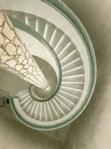 A spiral staircase with a marble-like stone appearance, set in a well-lit, elegant space with classic architectural details