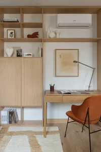A well-lit home office with a wooden desk, chair, bookshelf, and lamp, set against a white wall and wooden floor