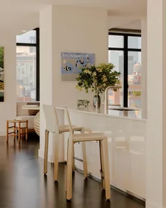 Well-lit kitchen with a white countertop, sink, dining table, and chairs, featuring a vase and potted plant