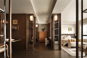 A well-lit bedroom with a wooden floor, a bed, a dresser, and a chair, creating a bright and inviting atmosphere