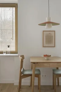 Dining room with a wooden table and chairs, set with a bowl of fruit and a vase, in a bright and inviting space with a white color scheme