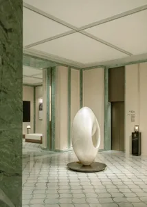 A large white sculpture on a pedestal in a dimly lit room with a marble floor, surrounded by a contemporary art gallery setting