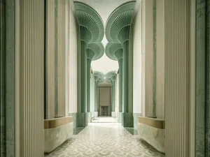 A long, narrow, modern hallway with green walls, arched doorways, and natural light from above, creating a peaceful atmosphere