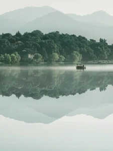 A serene lakefront house with a boat floating in the water, surrounded by trees