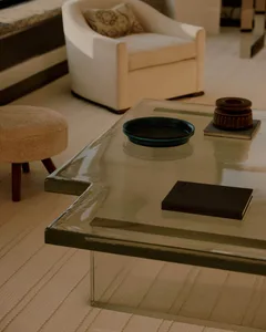 A well-lit living room with a glass coffee table, a couch, a chair, and a book, creating a cozy atmosphere
